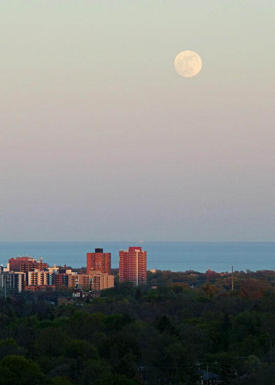 full moon at dusk over a lake and city horizon