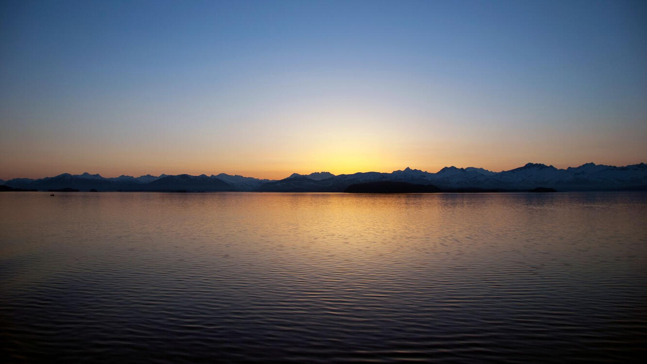 the sun setting behind distant mountains on a lake