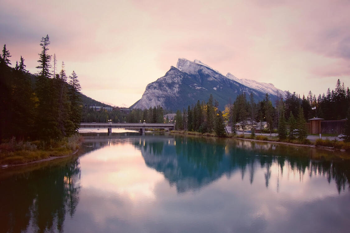 a mountain and its reflection on a still river during a sunrise of purple skies