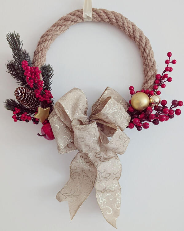 Christmas wreath made of jute rope with artificial berries, spruce needles, and a big gold bow