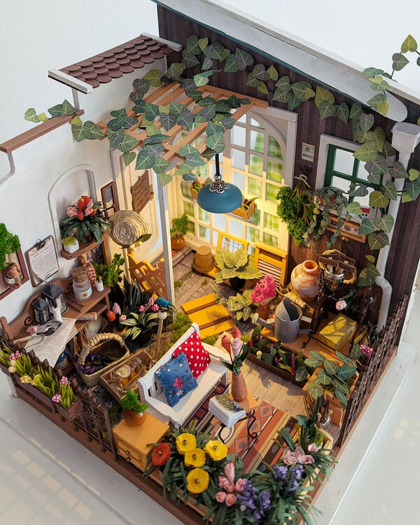 miniature model garden made of paper and wood, with sitting and potting areas and vine growing along the wall