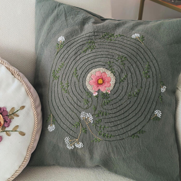 green pillow with an embroidered labyrinth pattern with flower and leaf motifs