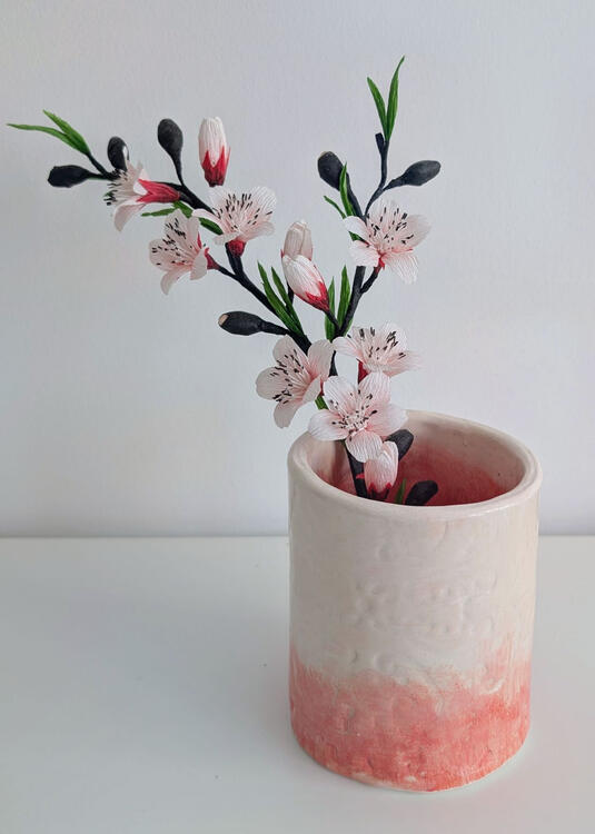 white and pink ceramic cylindrical vase holding a branch of crepe paper cherry blossoms