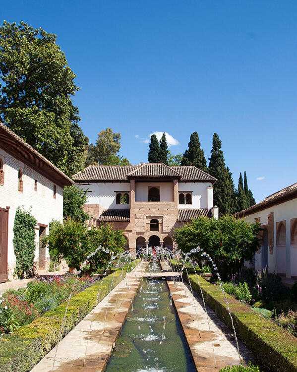a 13th century Islamic courtyard garden with a long central pool, fountains, flower beds, and architectural arcades