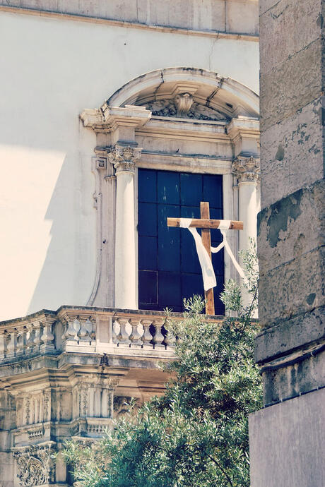 wooden cross with white cloth blowing in the wind on historical balcony