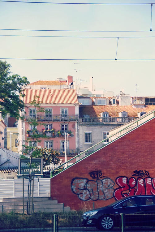 a black car passing by a red brick wall with graffiti with apartment buildings in the background