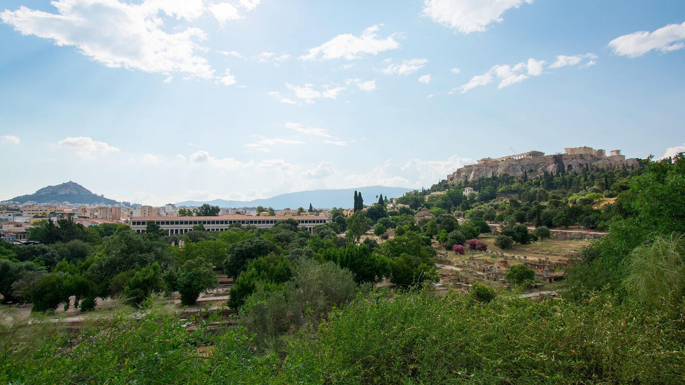 view overlooking a large field with ancient ruins and the Acropolis in the background