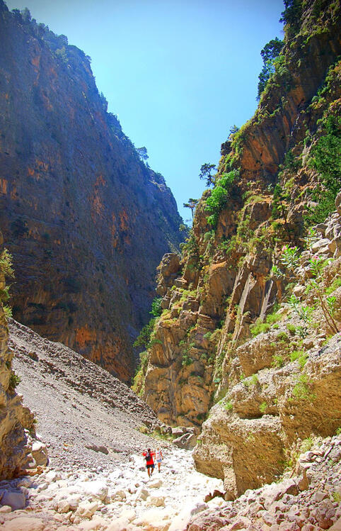 two people hiking in a rocky valley between steep, rocky mountains